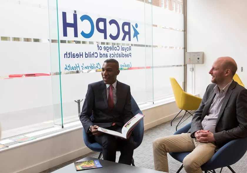 Two men talking in building lobby, with RCPCH logo (reversed) on outside window