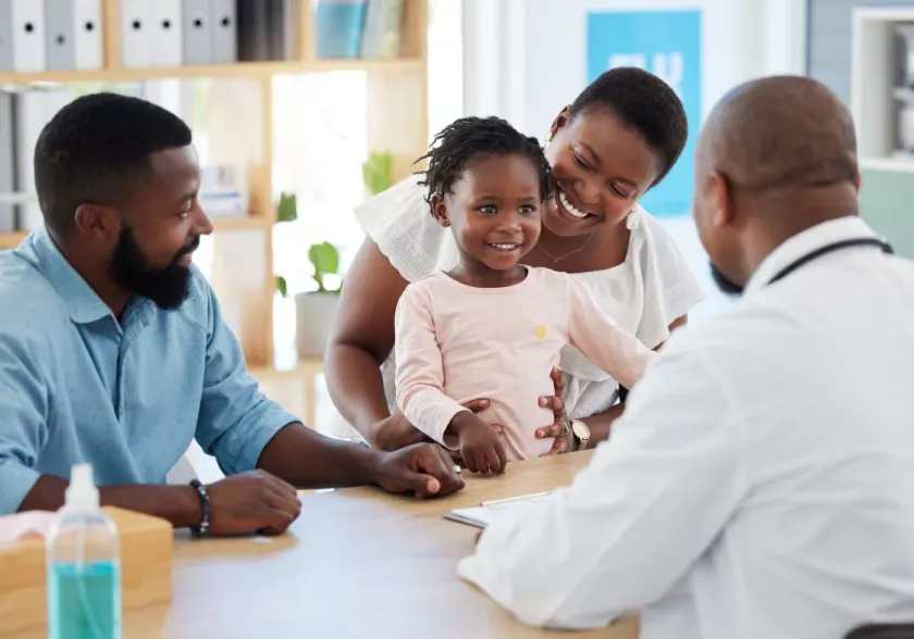 Man and woman, with toddler, smiling, meet with a doctor
