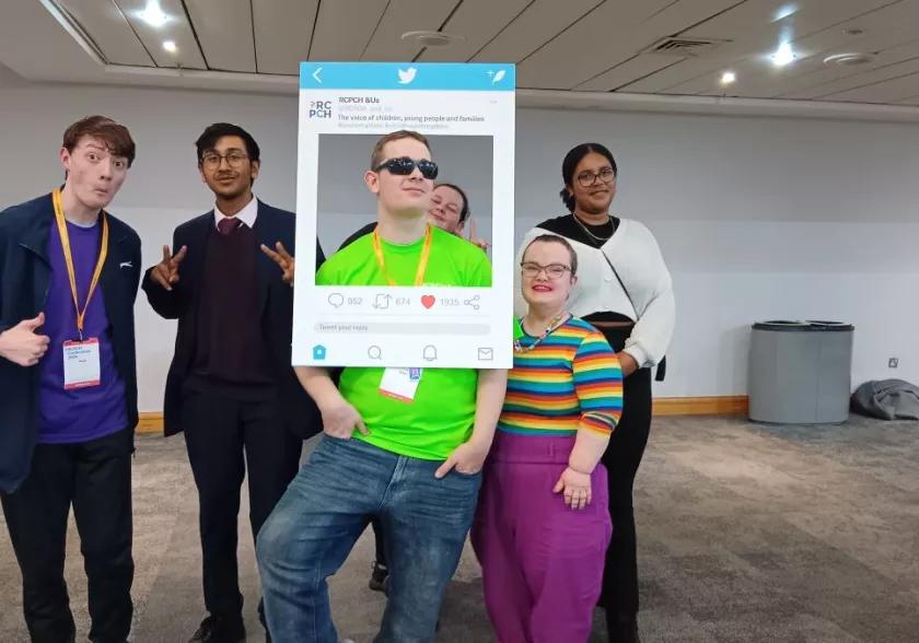 Group of young people posing with an RCPCH &Us cardboard card at a conference