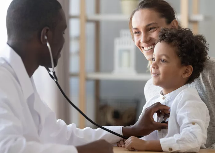 Doctor listens with stethoscope to heart of toddler held by mum