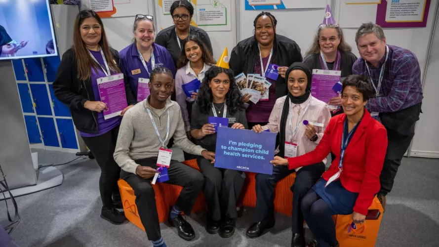 A group of people sitting and standing, holding a card that reads "I'm pledging to champion child health services" and holding materials celebrating Purple Day for epilepsy