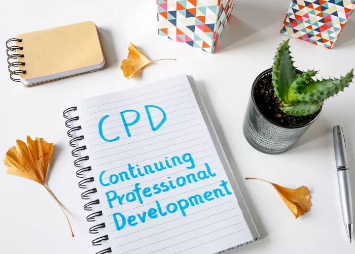 Notepad with handwritten 'CPD Continuing Professional Development' on a desk with plant and stationery