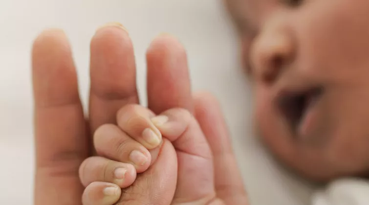 Young baby sleeping with hand in adult's hand