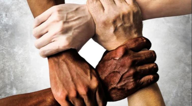 Four hands of different skin tones holding each other in a square