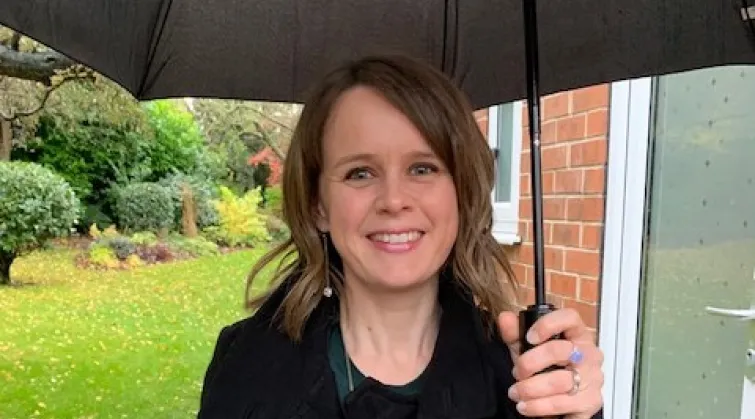 Anne Pinches, smiling, under large umbrella