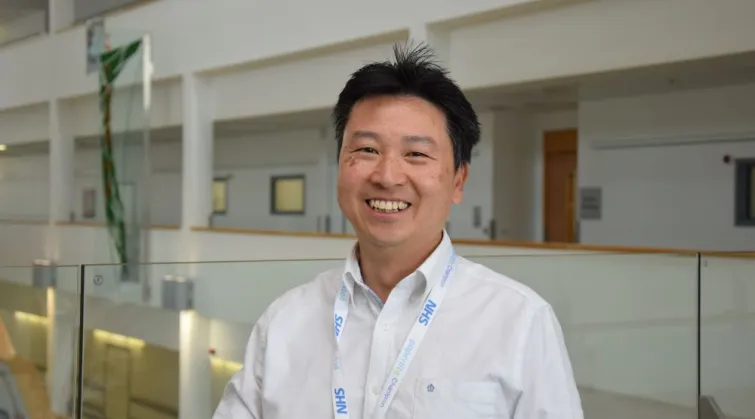 Photo of Dr Yincent Tse, wearing an NHS lanyard, at a conference centre