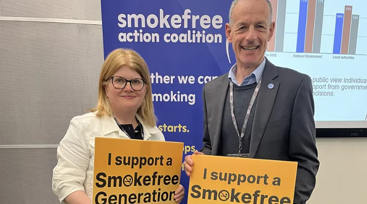 Two people holding up signs that read 'I support a Smokefree Generation', in front of a banner reading 'smokefree action coalition'