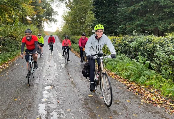 A group of cyclists, including Camilla, coming towards the camera on a small country road