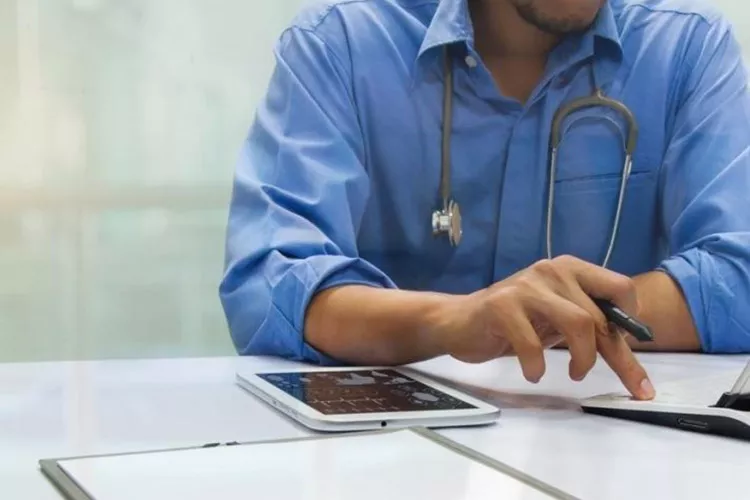 Man wearing stethoscope at computer and tablet