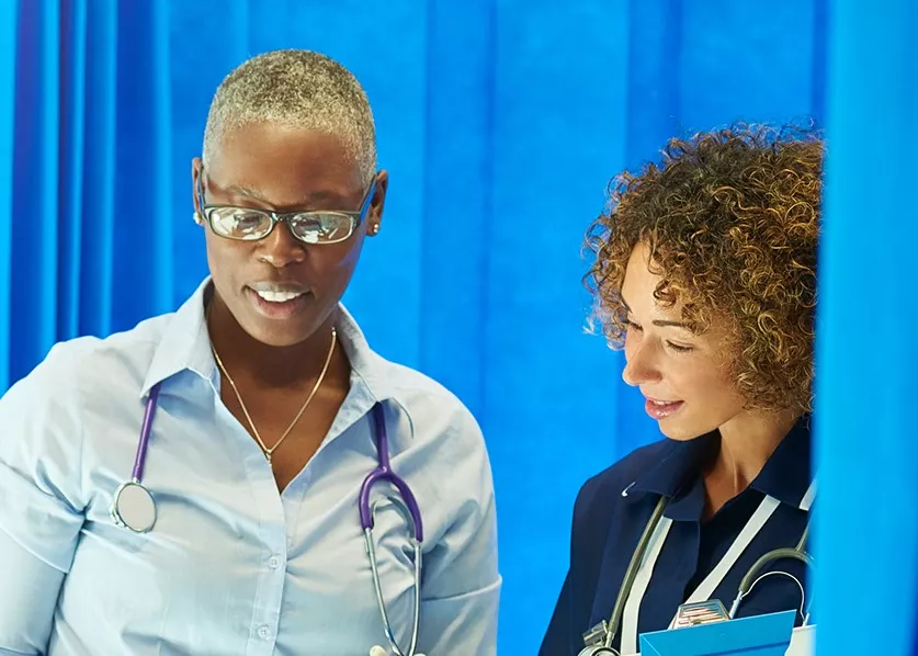 Two health professionals talking in front of a hospital curtain