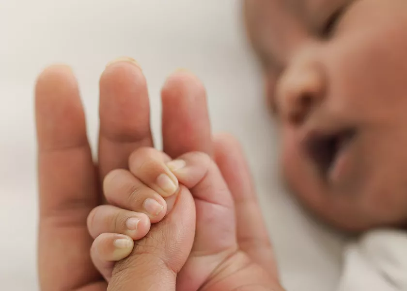 Young baby sleeping with hand in adult's hand