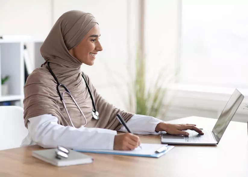 Young woman doctor with stethoscope working on computer