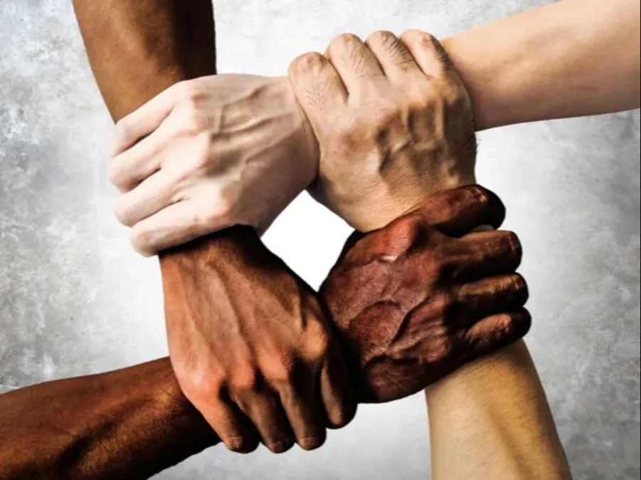 Four hands of different skin tones holding each other in a square