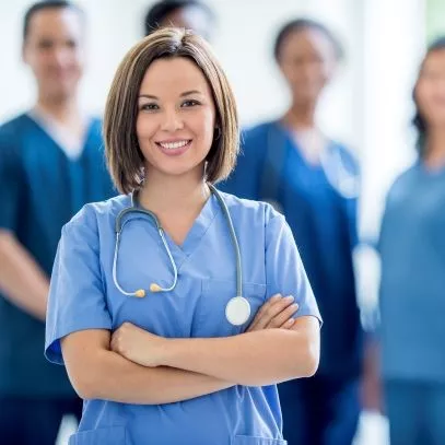 Health professional wearing scrubs and stethoscope stands in front of other health professionals 