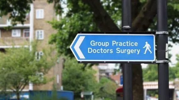 Directional street sign reading 'Group Practice Doctors Surgery' in front of residential building