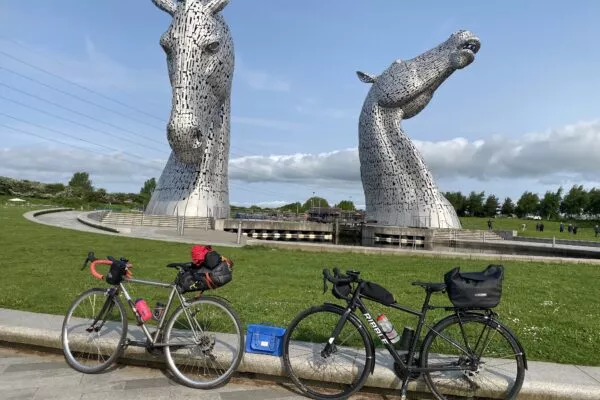 Two cycles parked in front of sculpture of horses