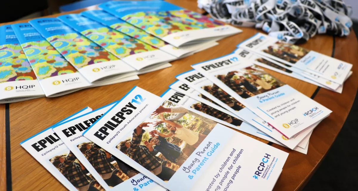 A table with Epilepsy12 leaflets, reports, and lanyards laid out
