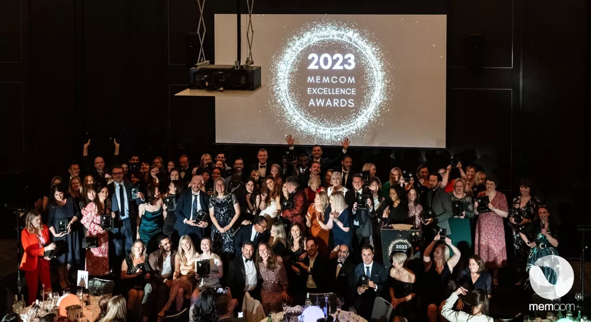 Group of people at awards ceremony, with large sign reading 2023 Memcom Excellence Awards
