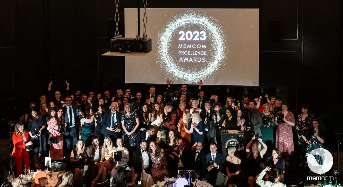 Group of people at awards ceremony, with large sign reading 2023 Memcom Excellence Awards