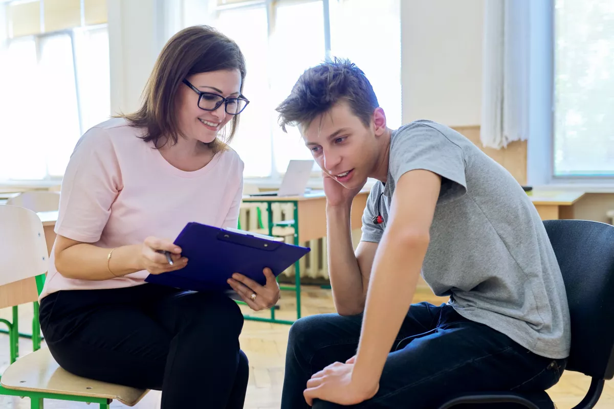 Woman health professional with a clipboard speaking with a teenage boy, in a school or community centre