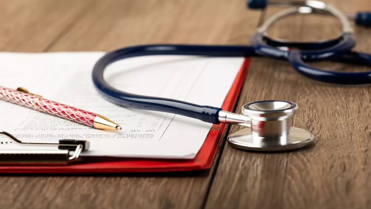 Stethoscope with clipboard, paper and pen on a wooden surface
