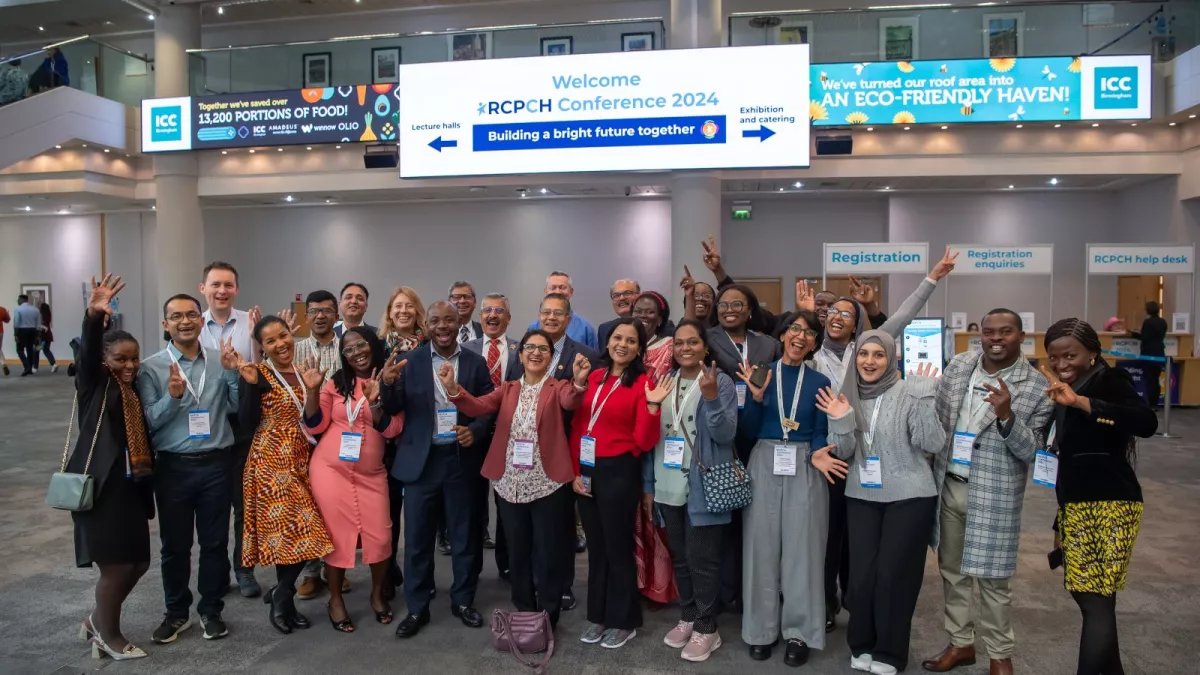 Group of people standing and smiling, with RCPCH Conference registration desks behind
