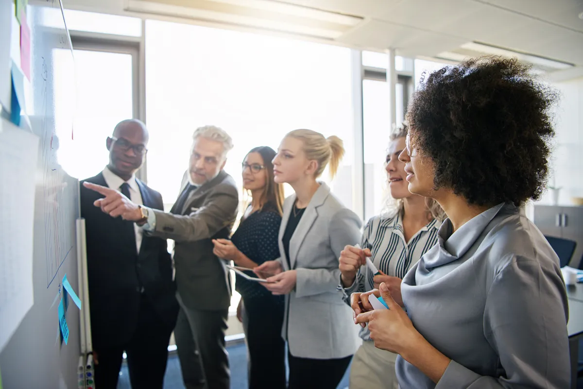 Group of people looking and pointing at whiteboard