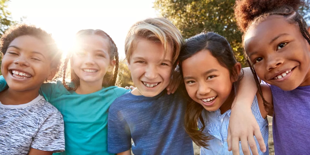 Five children standing in a line, smiling, with sunshine behind