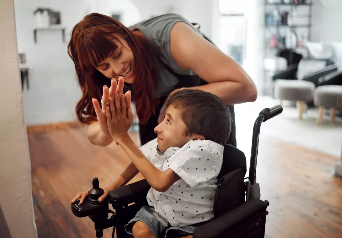 Child in a wheelchair high fives a woman, in a hospital setting