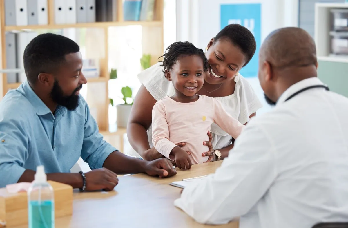Man and woman, with toddler, smiling, meet with a doctor