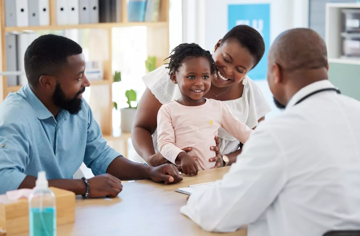 Man and woman, with toddler, smiling, meet with a doctor