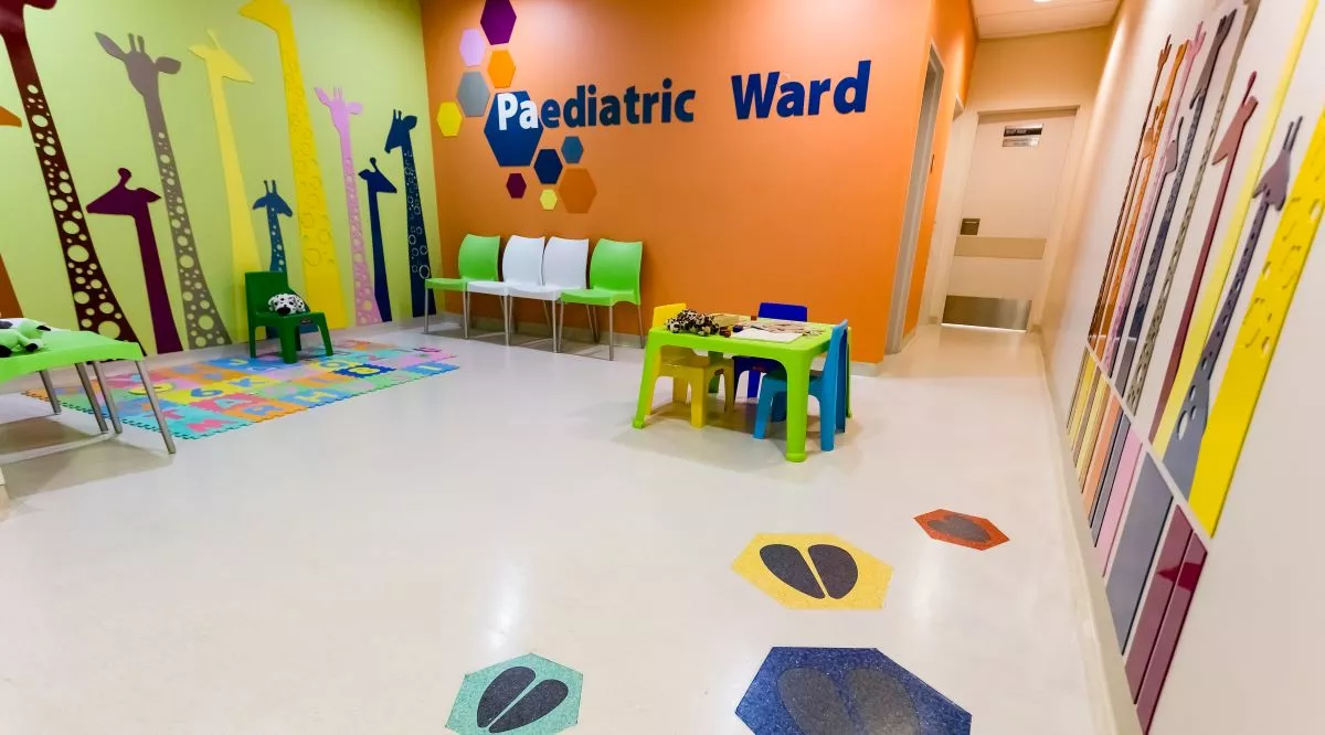 Inside of a children's hospital waiting area, with Paediatric Ward and animal stickers on colourful walls, plus toys and games