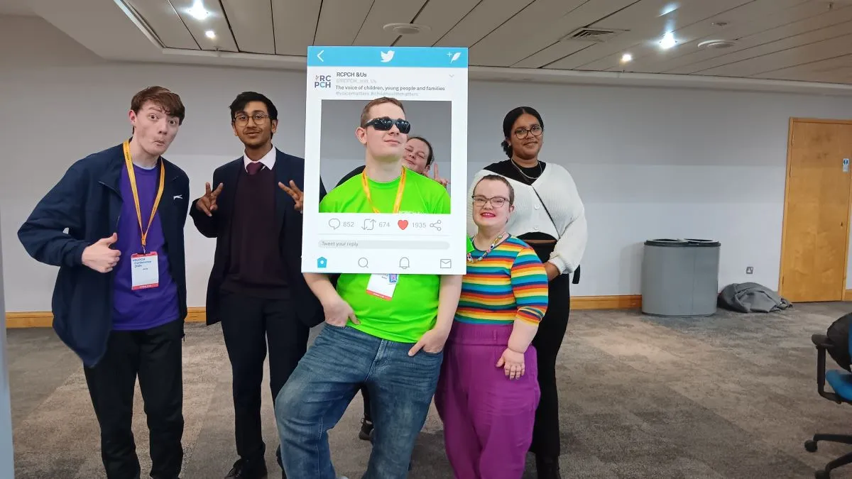 Group of young people posing with an RCPCH &Us cardboard card at a conference