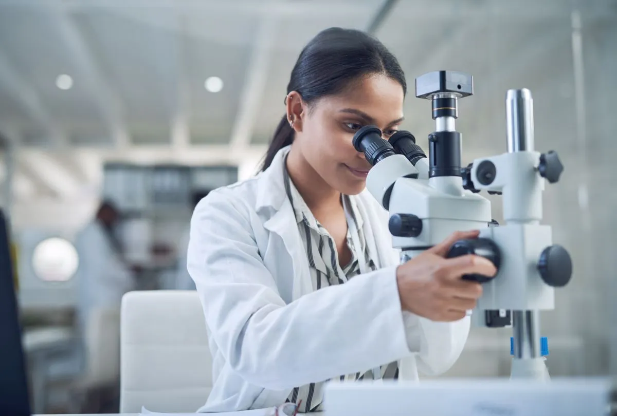 Woman in white coat looks into microscope in a laboratory