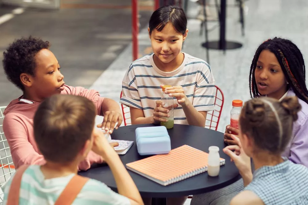 Older children around a table, drinking juice, with notebooks