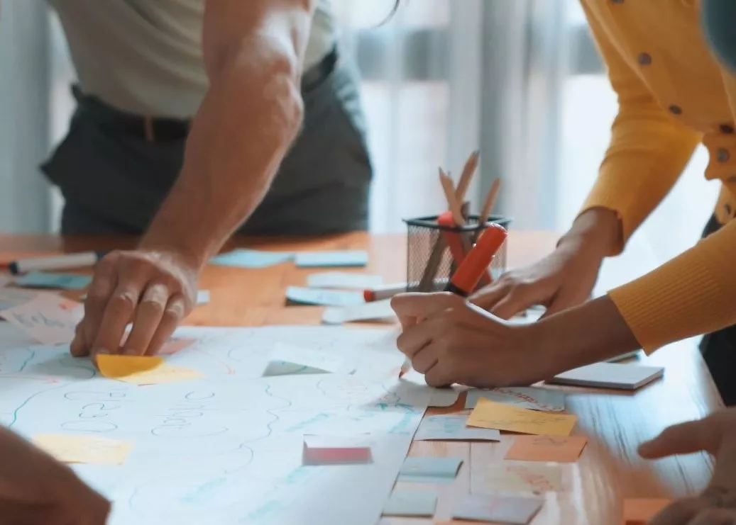 Close up of people around a table, using post-its on paper in a collaborative way