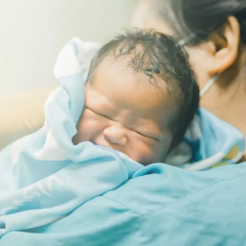 Small baby, being held by adult wearing scrubs and mask