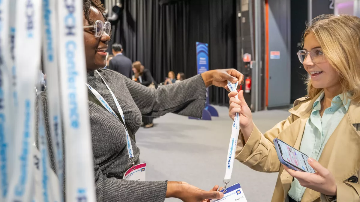 At RCPCH Conference, a staff member hands a delegate her badge and lanyard
