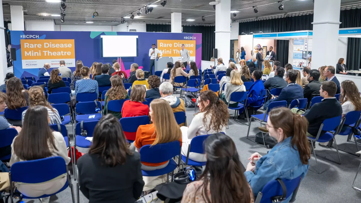 Rare disease hub mini theatre in an exhibition hall, with two presenters and lots of people listening