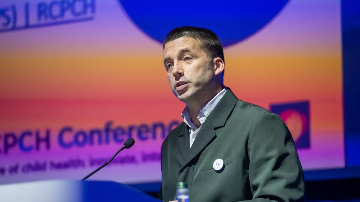 Man presenting on stage in front of a presentation slide