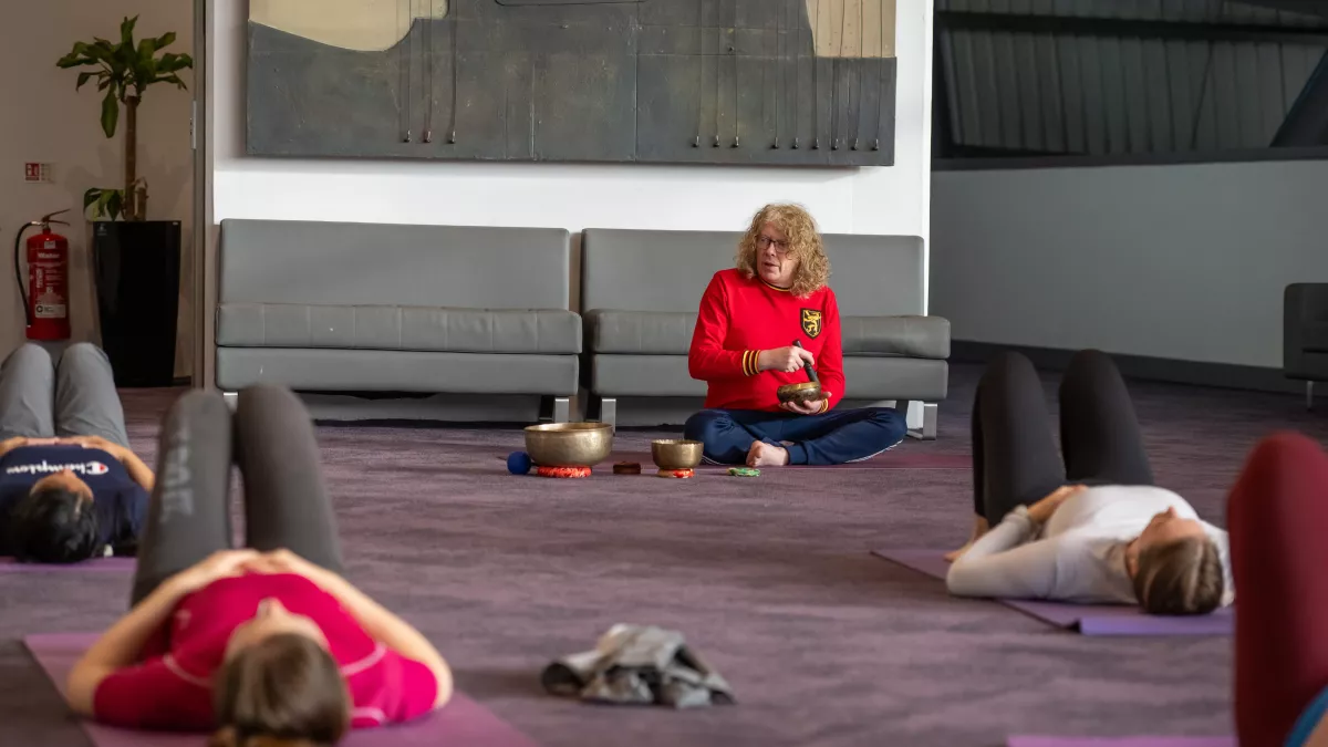 Man using singing bowls while others lie in relaxation at a yoga session