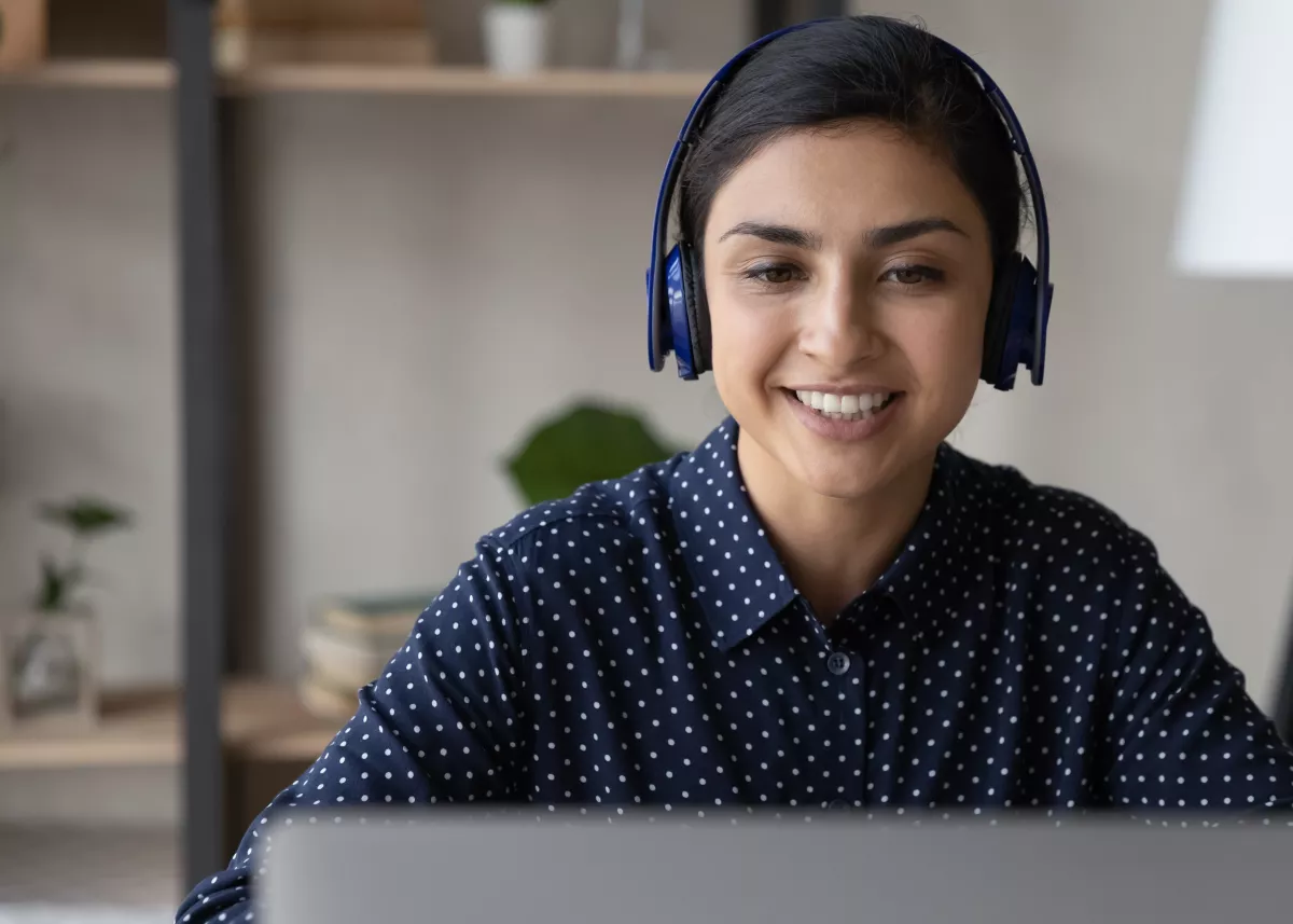 Woman wearing headphones while looking at a laptop, in a home office environment