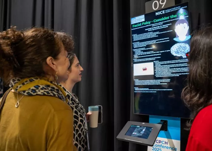 Three people looking at a digital screen of an abstract poster on facial palsy - at RCPCH Conference 2025