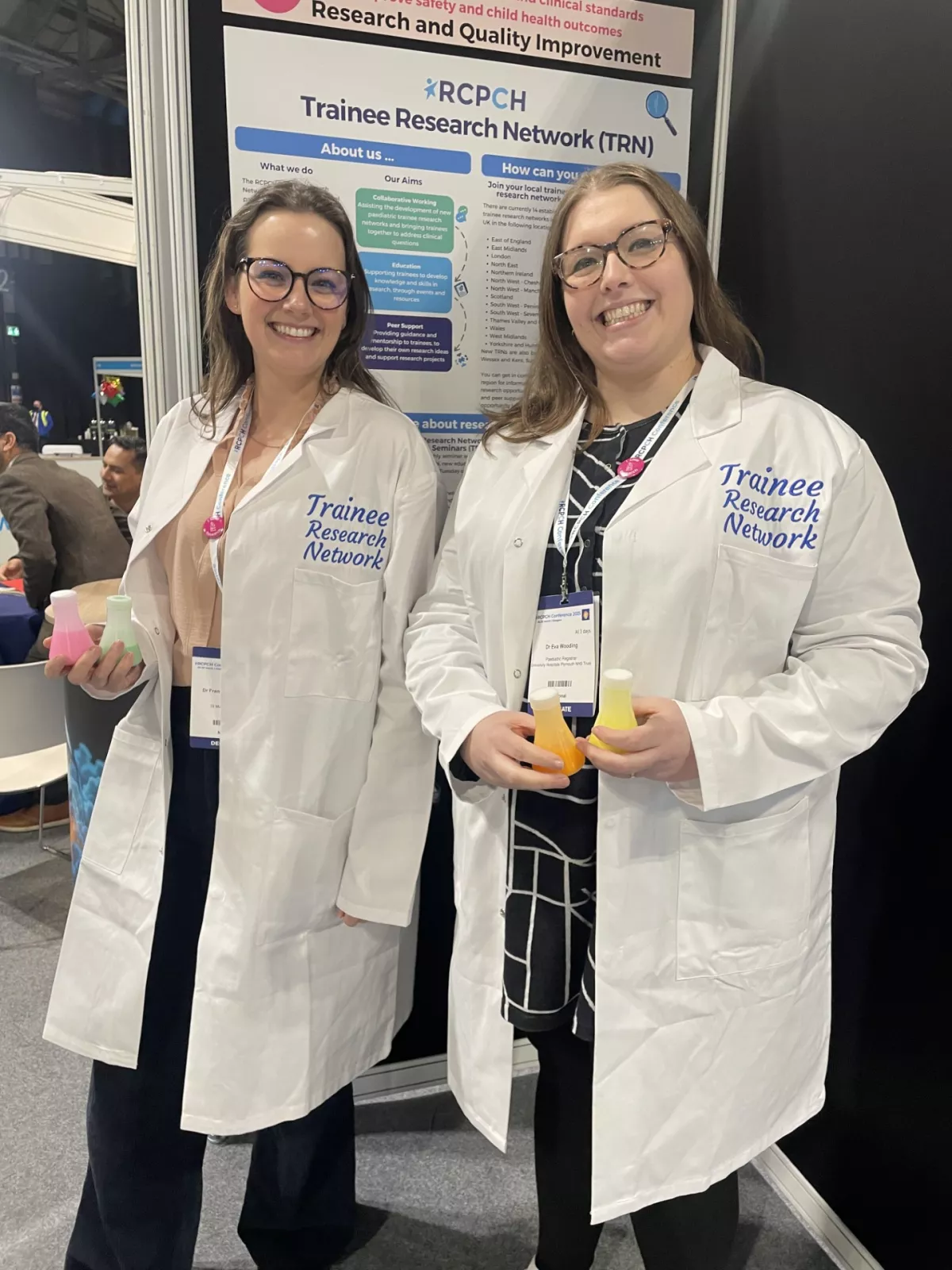 Two women wearing white lab coats reading Trainee Research Network