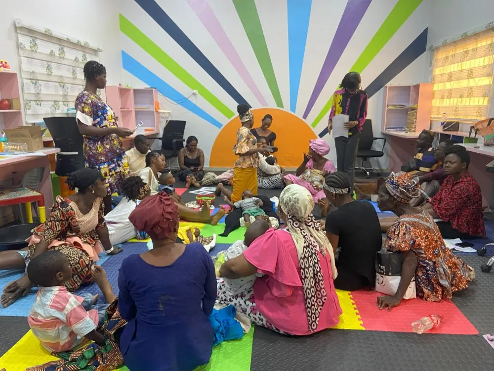 Group of women and babies sitting, in a brightly coloured room