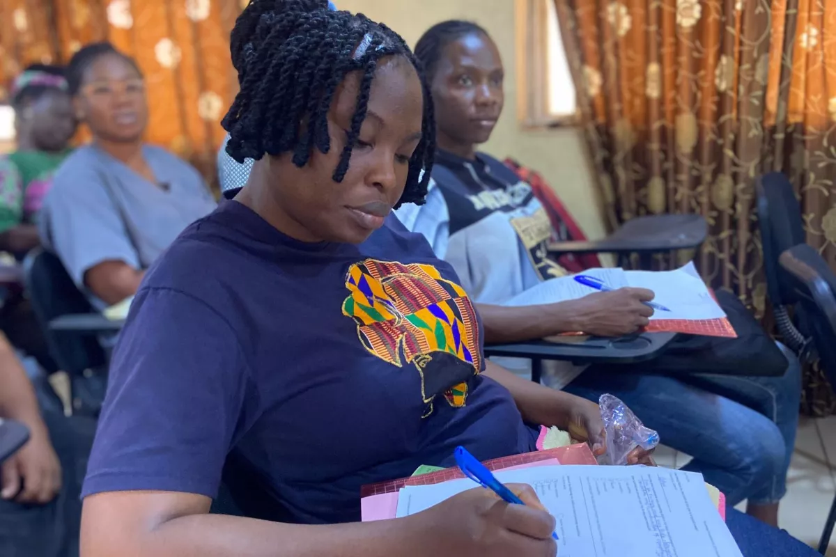 Classroom with woman seated at desk taking notes on paper, with others behind her
