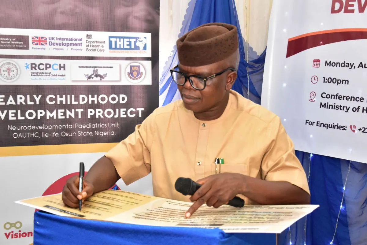 Man signing formal document, sign behind reads Early Childhood Development Project