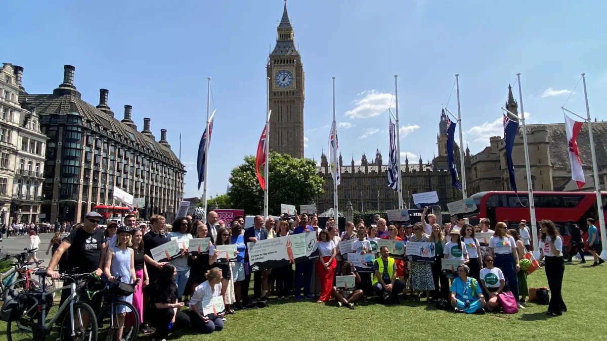 Group of people holding signs about Clean Air Day, some with bicycle, in front of Houses of Parliament