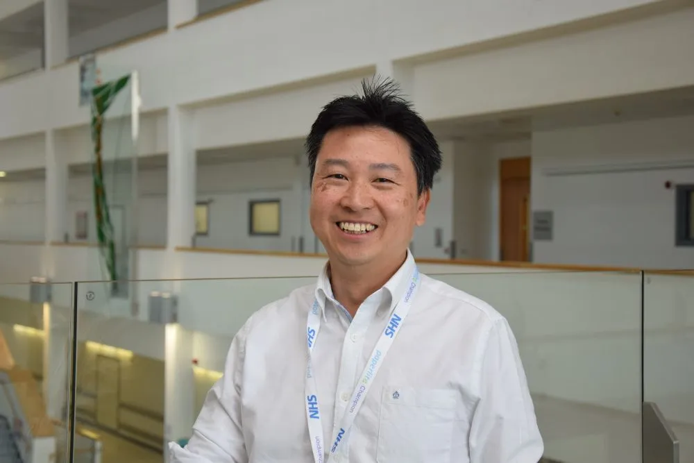 Photo of Dr Yincent Tse, wearing an NHS lanyard, at a conference centre