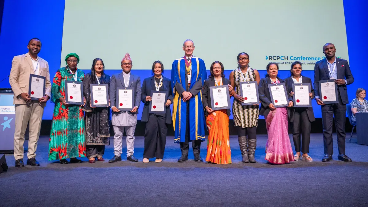 The Visiting Fellows holding up their certificates while standing on stage with RCPCH President